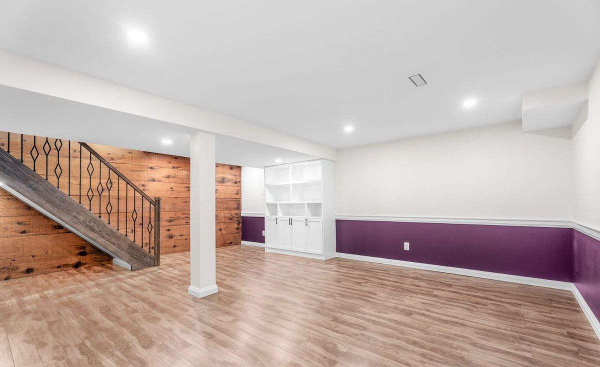 Finished basement with purple lower walls, white trim and a wood feature wall by the stairs
