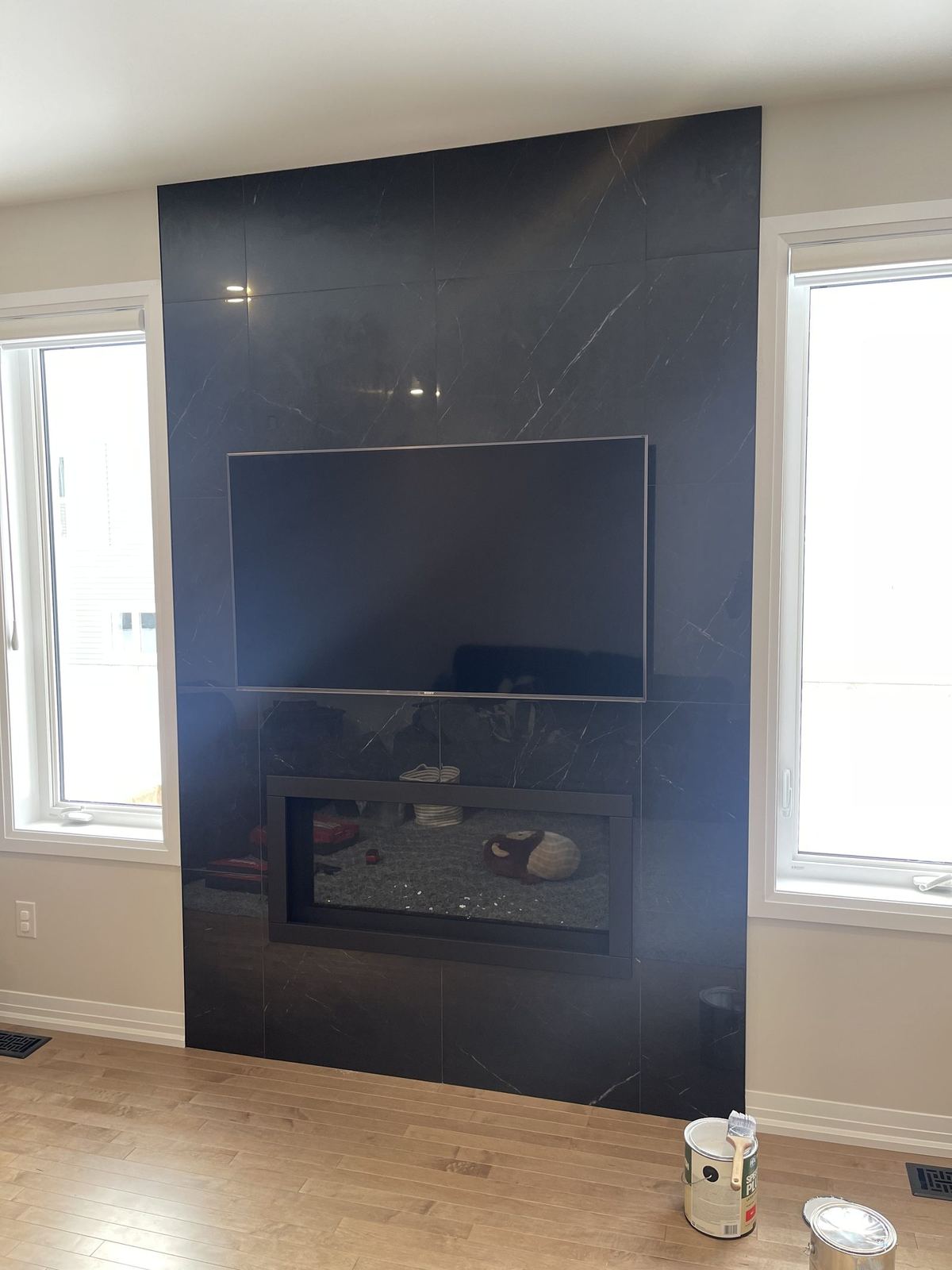 Living room with fresh light walls around a dark floor-to-ceiling fireplace wall, paint cans still on the floor